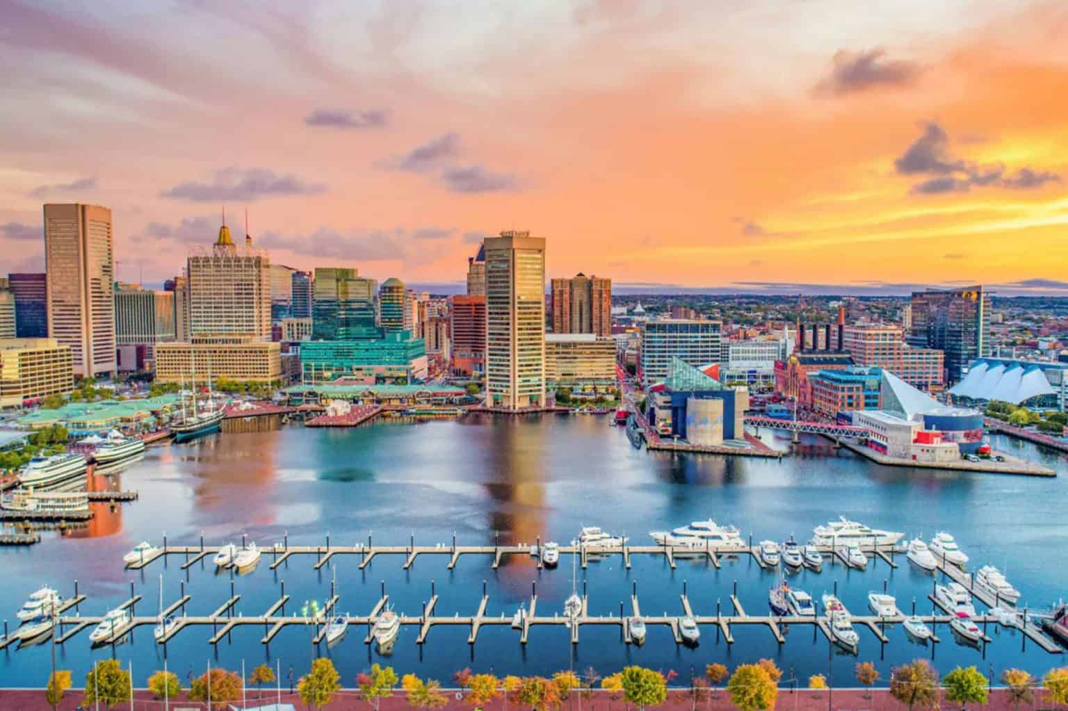 Aerial view of Baltimore, Maryland, showing a vibrant sunset and city skyline near a port.